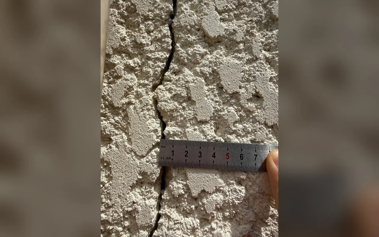 Fissure dans un enduit rugueux, avec un mètre gradué posé en travers pour donner l'échelle.