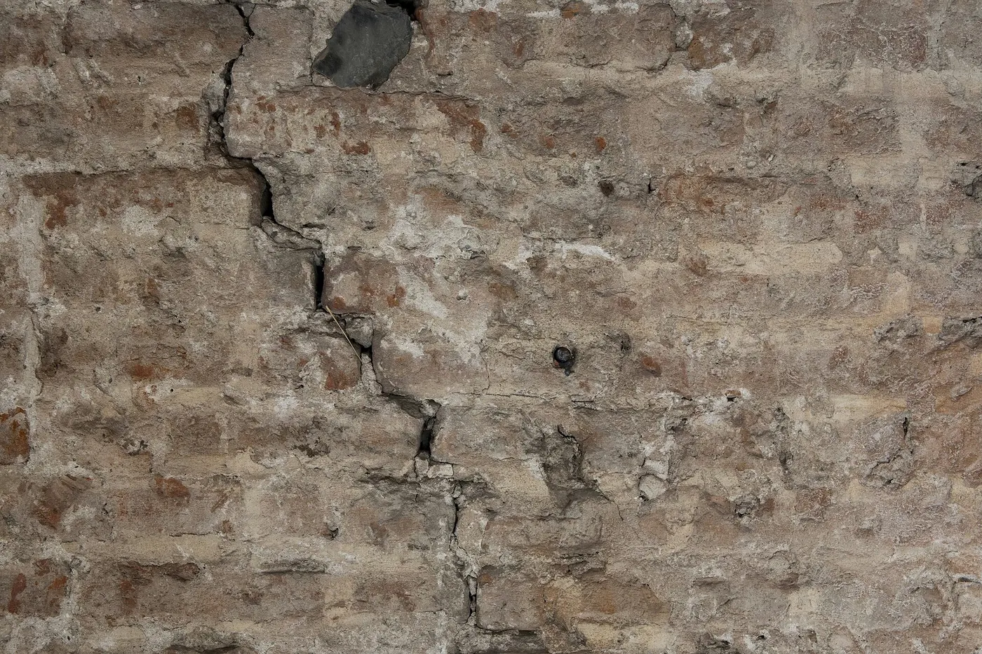 Mur de briques anciennes traversé par une fissure en zigzag qui suit les joints de mortier.