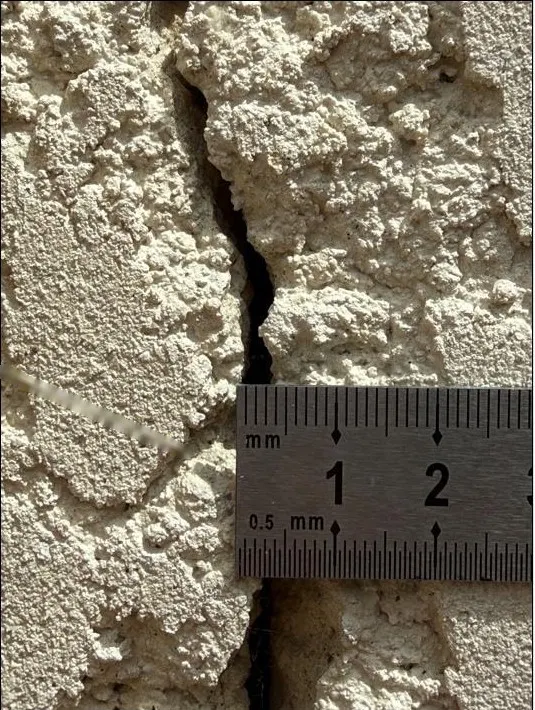 Fissure dans un enduit rugueux, avec une règle graduée posée en travers pour mesurer sa largeur.
