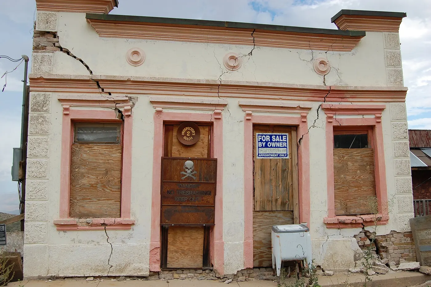 Façade d'un petit bâtiment aux murs traversés par de larges fissures.