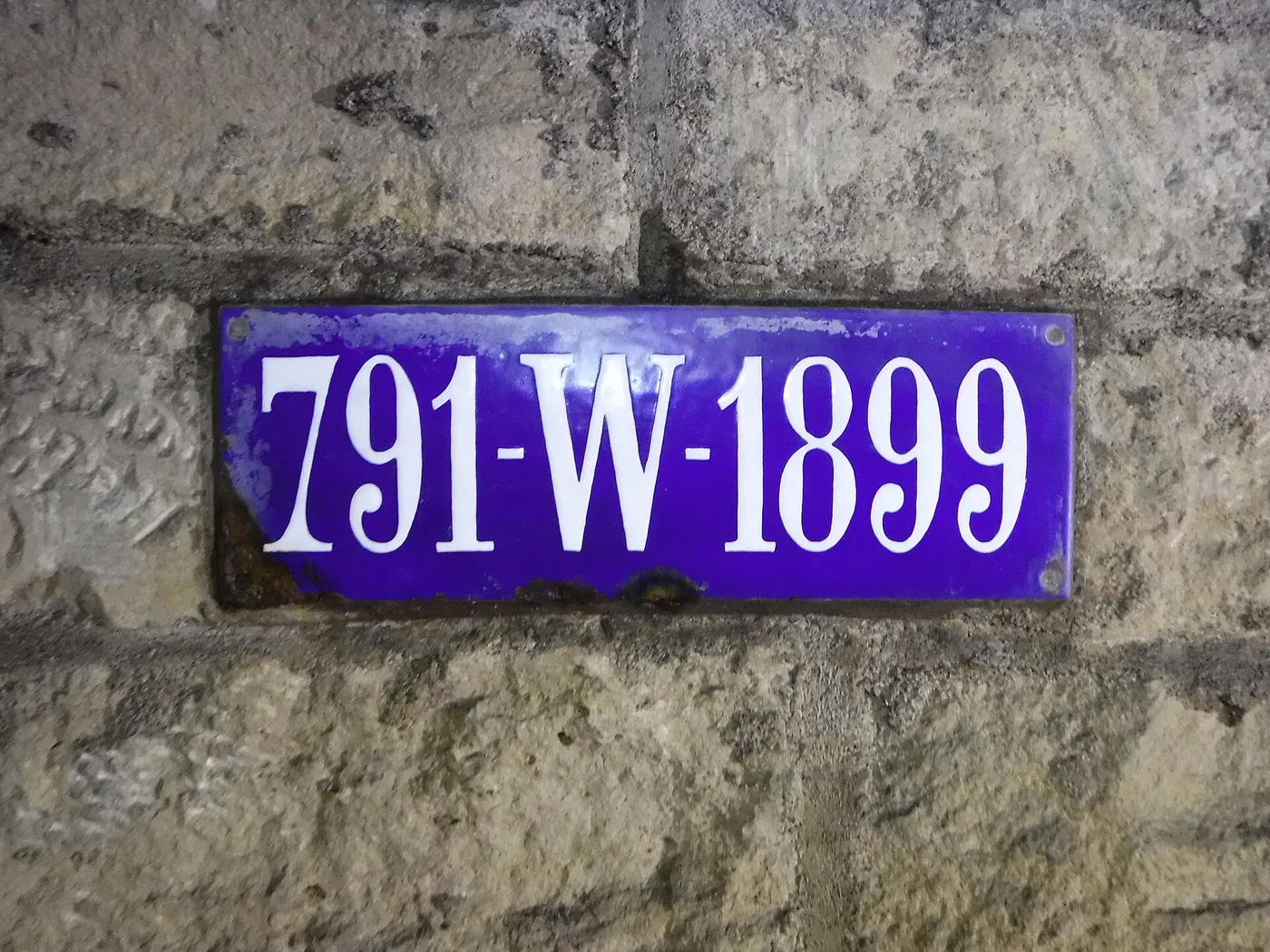 Plaque émaillée bleue portant le numéro 791-W-1899, fixée sur un mur de pierre dans une galerie souterraine.