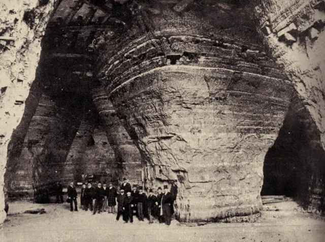 Photographie ancienne de visiteurs au pied de piliers de gypse dans une carrière, avec des rails au sol.