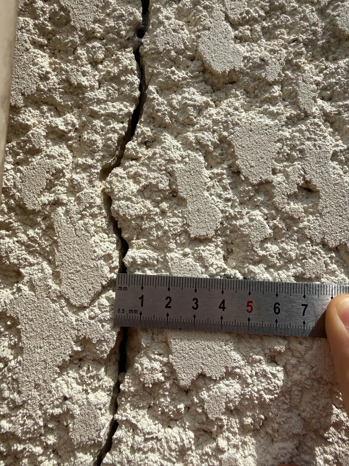 Fissure verticale dans un enduit rugueux, avec un mètre gradué posé en travers pour donner l'échelle.