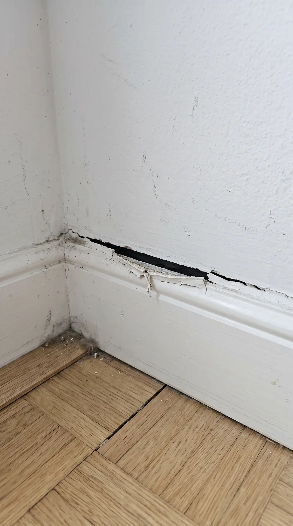 Illustration d'un angle de pièce où la plinthe se décolle du mur et laisse apparaître un jour sur le parquet.